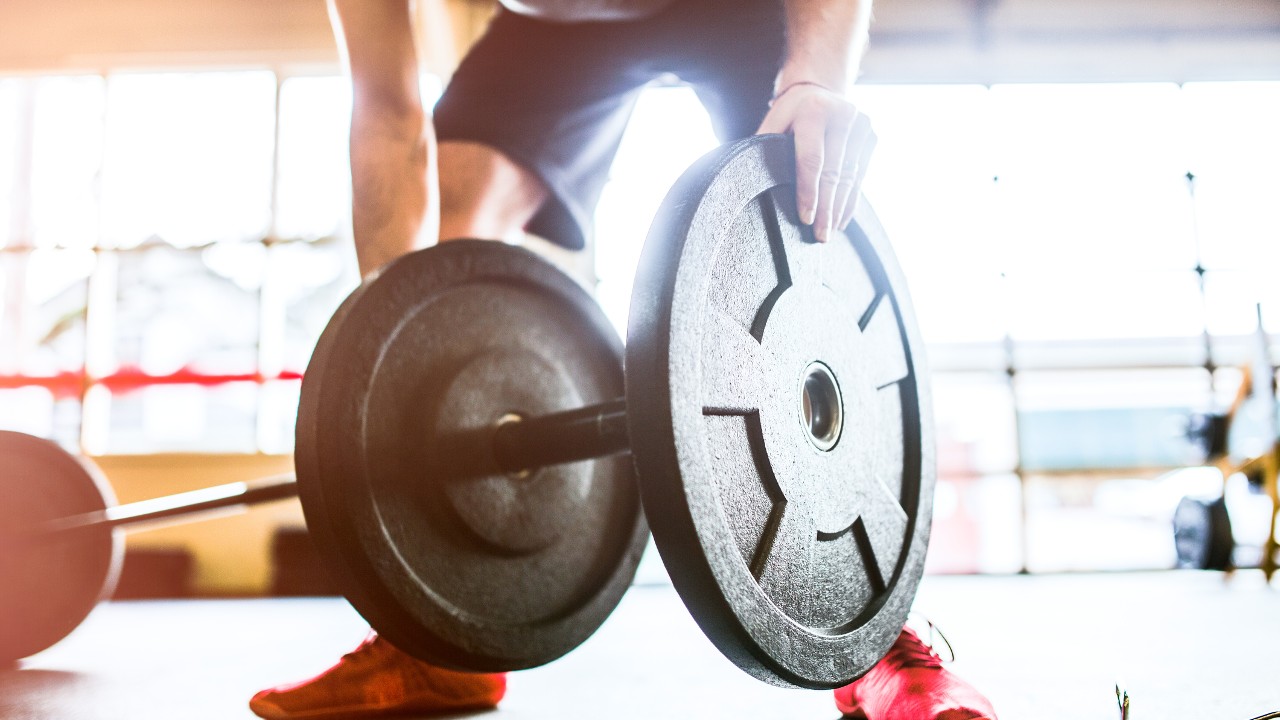 A man loads weight plates onto a barbell before beginning his gym workout routine