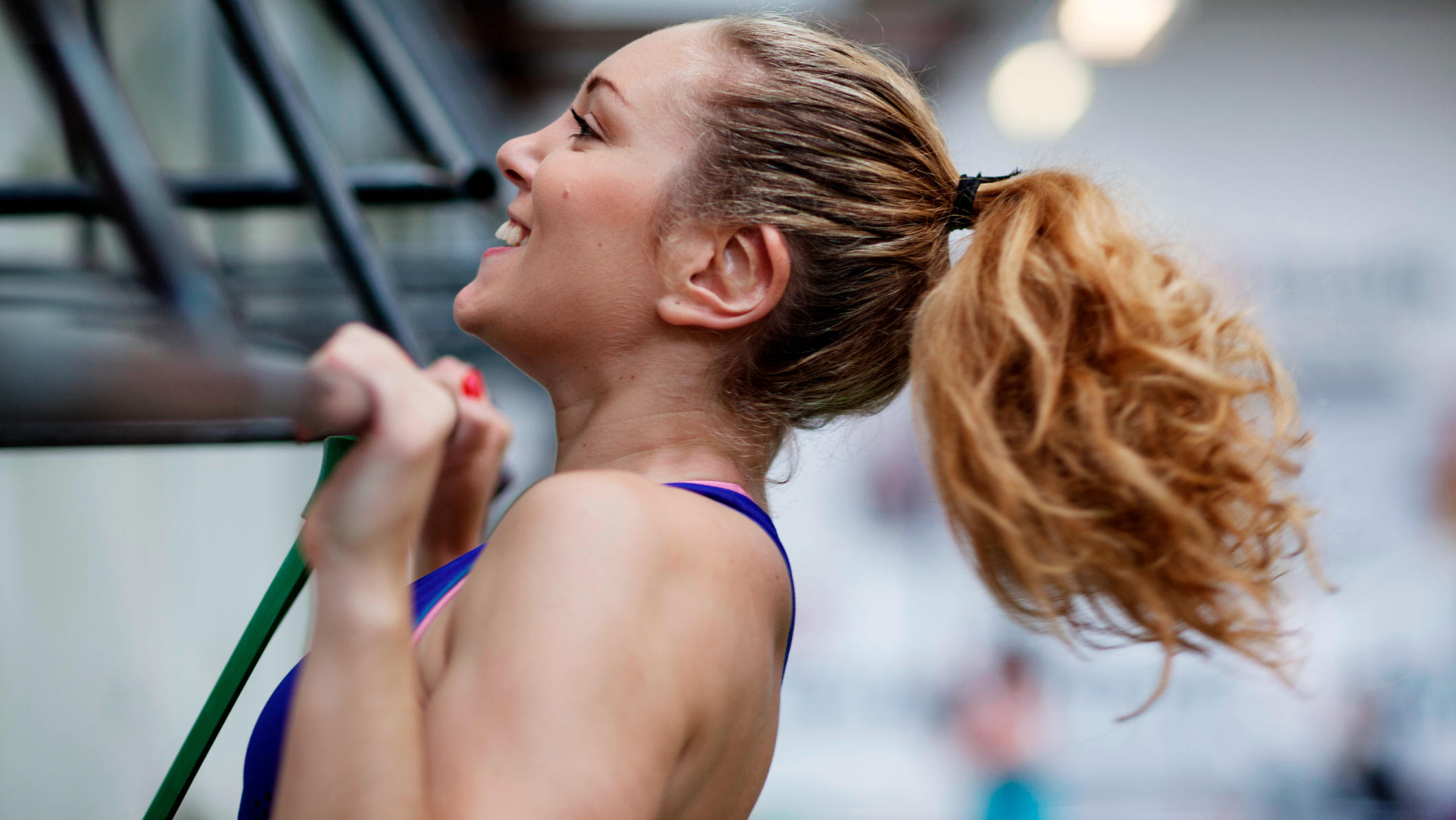Close-up of woman&rsquo;s head performing a pull-up, with her chin over the bar